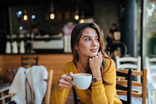 Stylish young woman drinking coffee at the cafe, looking away.