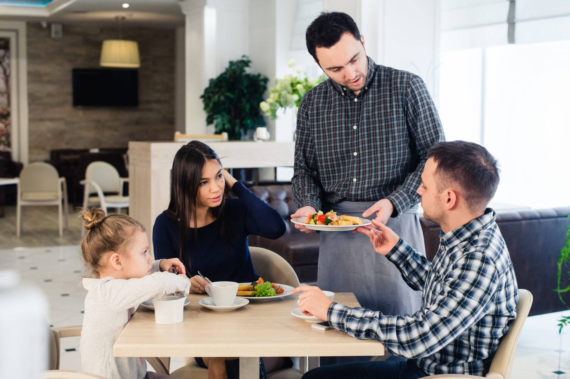 Waiter serving family in a restaurant and bringing full plate